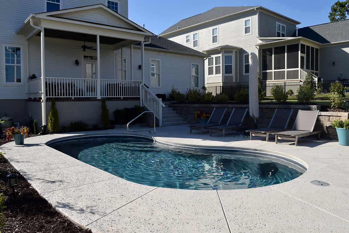 The image shows a backyard with an inground swimming pool, sun loungers, a well-maintained lawn, and a two-story house with a porch.