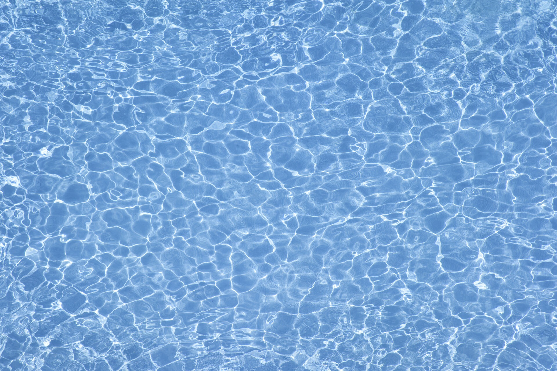 The image shows a close-up of calm, shimmering blue water with sunlight creating a pattern of wavy lines and ripples on the surface.